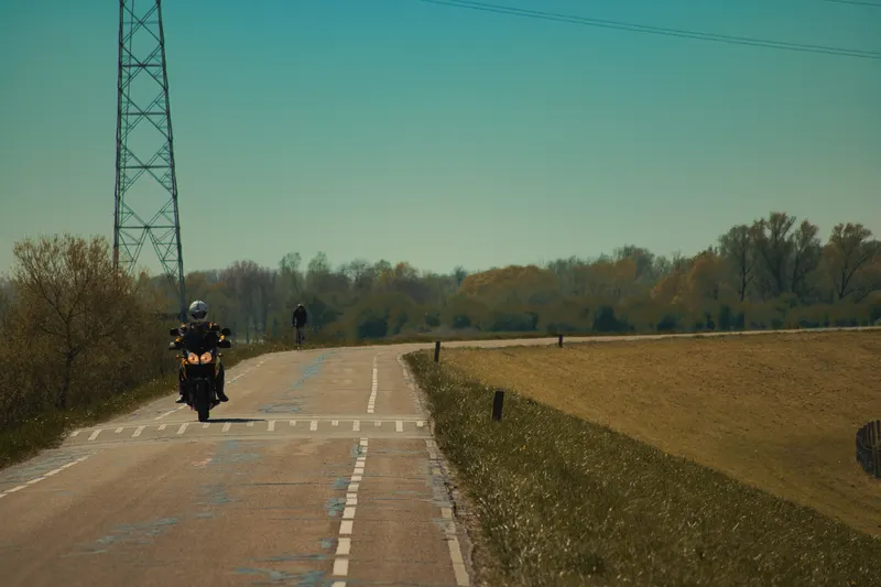A motorcyclist rides along a dike road past a high-voltage pylon