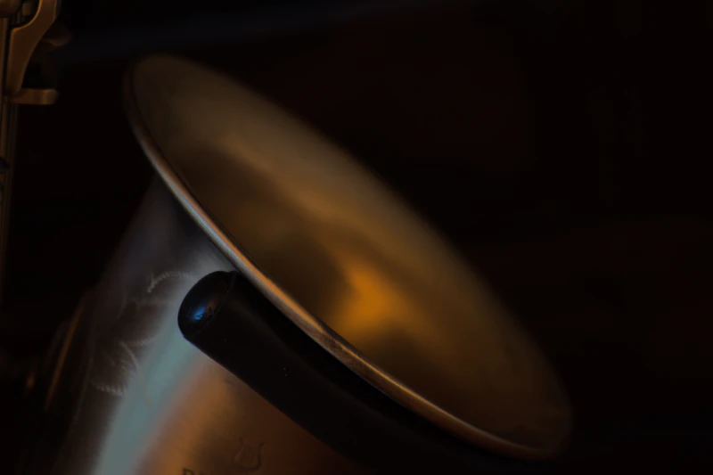The rim of a saxophone bell catching warm light against a dark background