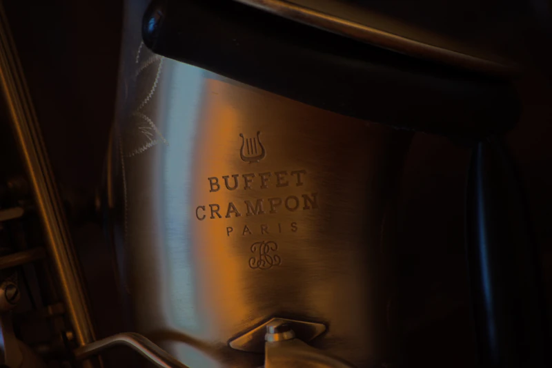 Close-up of the engraved Buffet Crampon Paris logo on a saxophone, in warm low light
